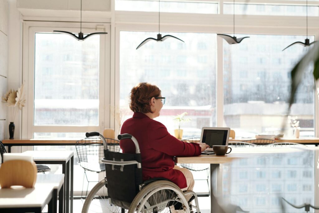 Jeune femme en fauteuil roulant travaillant sur son ordinateur portable à table dans un cadre lumineux