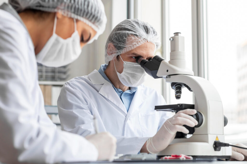 Laborantin travaillant sur un microscope accompagné d'une seconde personne prenant des notes