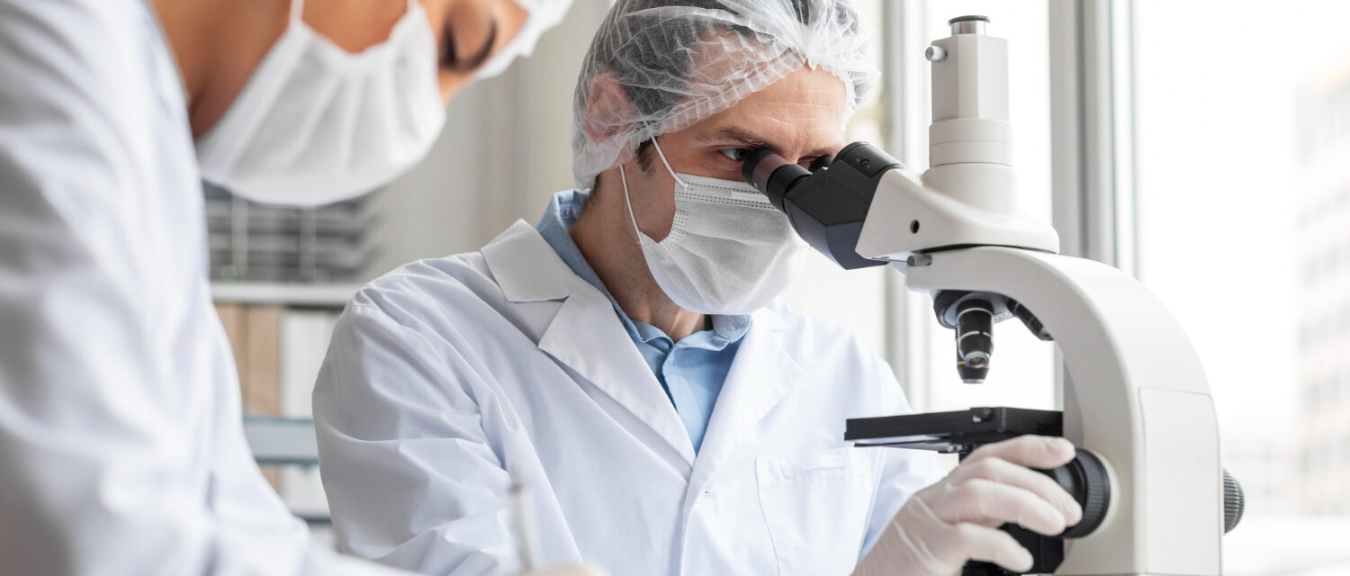 Laborantin travaillant sur un microscope accompagné d'une seconde personne prenant des notes