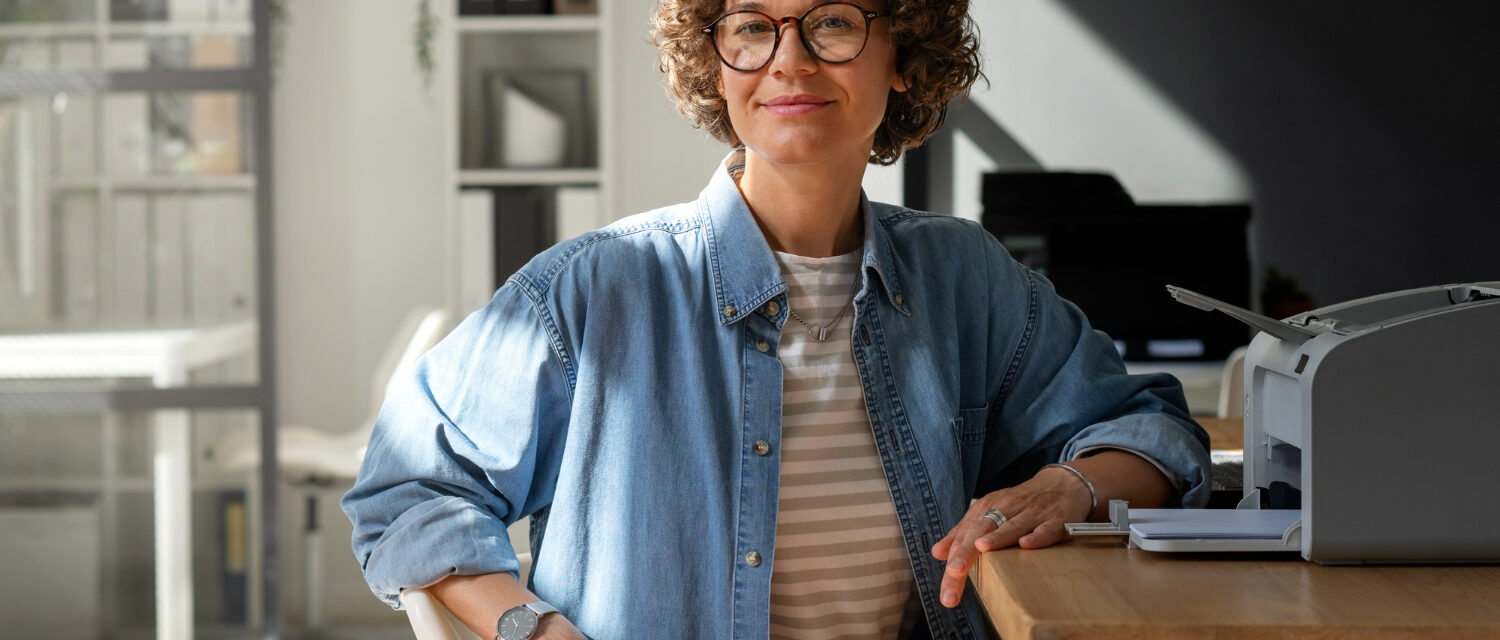 Femme avec une veste bleu en denim, assise à un bureau et regardant l'objectif