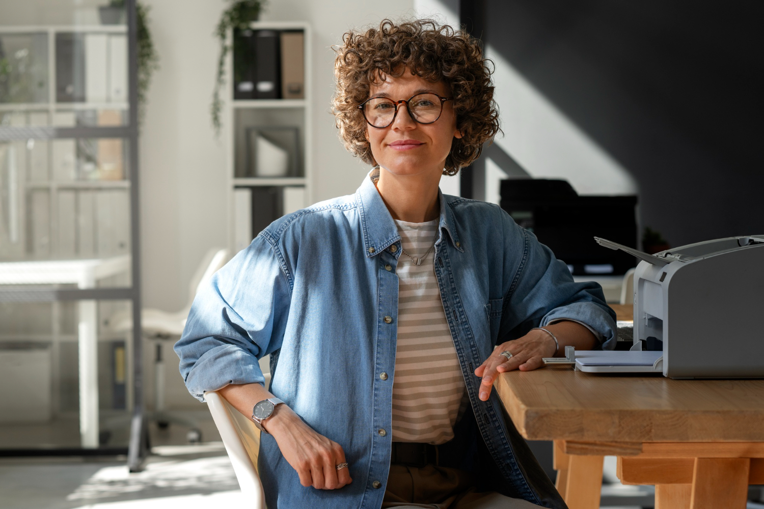 Femme avec une veste bleu en denim, assise à un bureau et regardant l'objectif