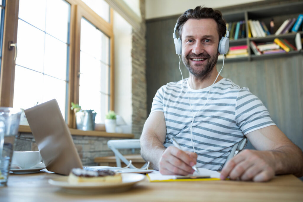 Homme avec un casque blanc prenant des notes devant son ordinateur et regardant l'objectif
