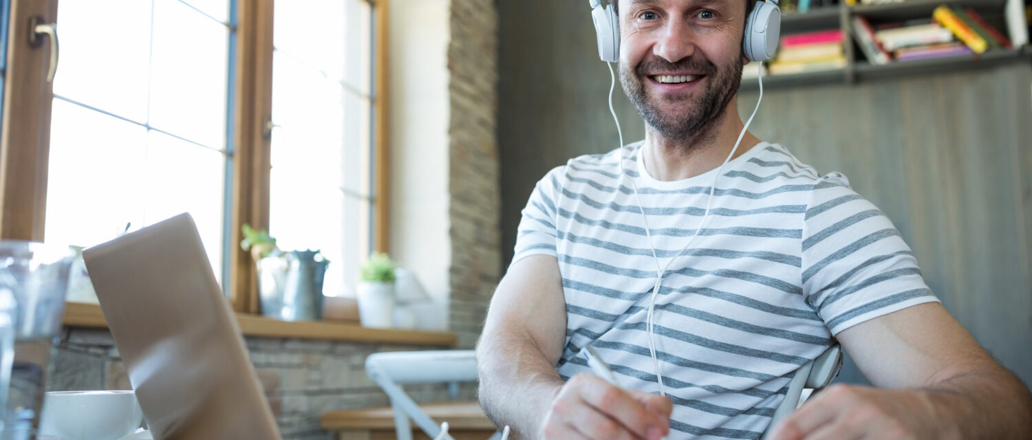 Homme avec un casque blanc prenant des notes devant son ordinateur et regardant l'objectif
