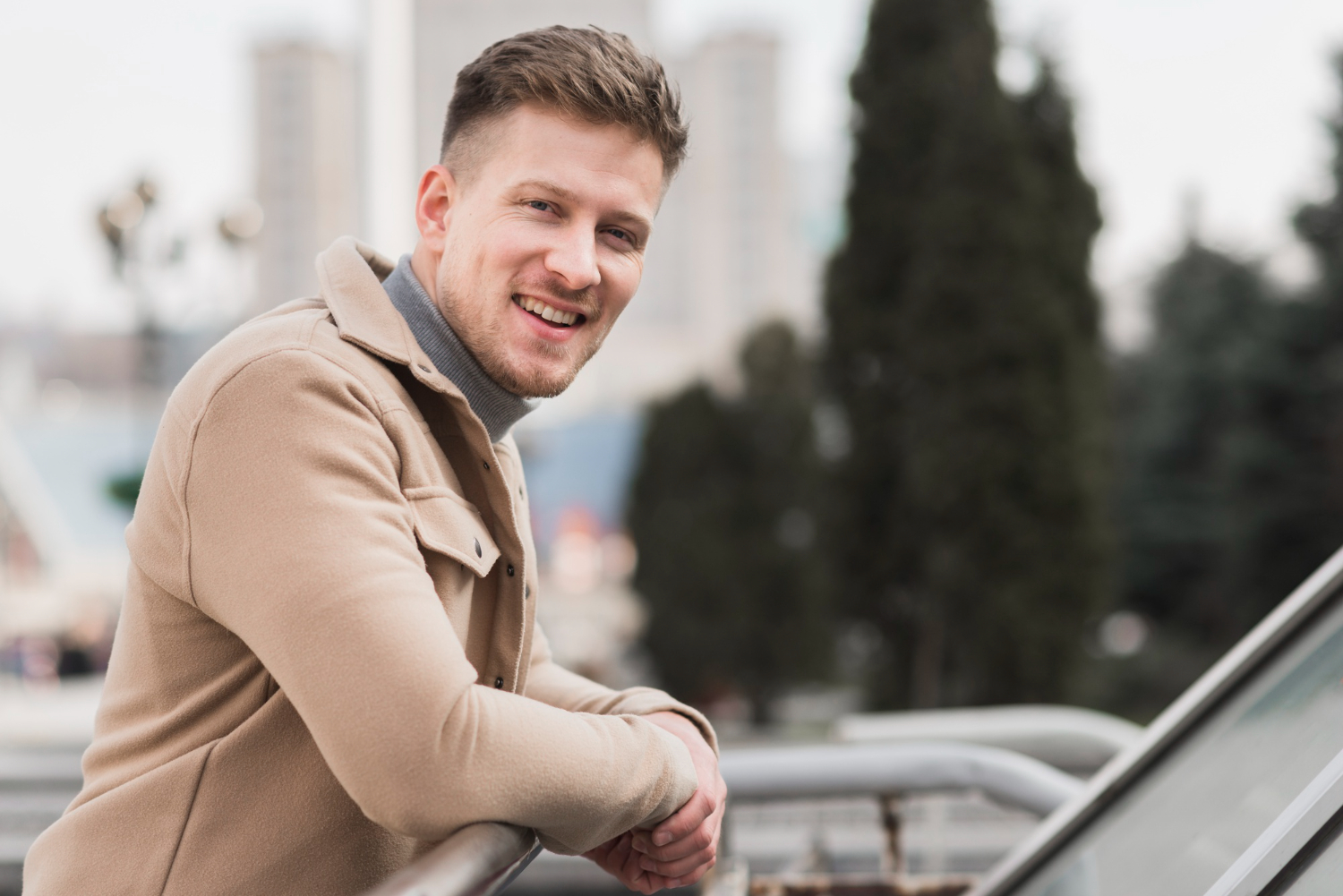 Homme accoudé à une rambarde en extérieur, souriant et regardant l'objectif