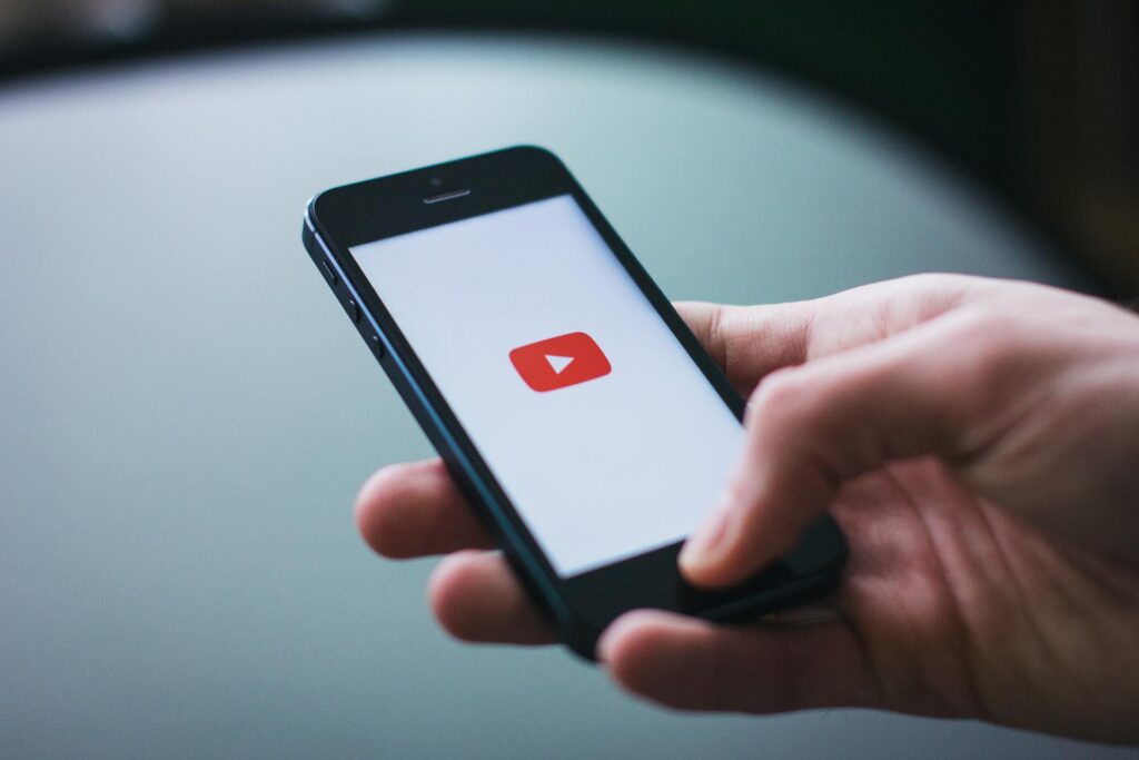 Main tenant une téléphone affichant le logo Youtube sur fond blanc